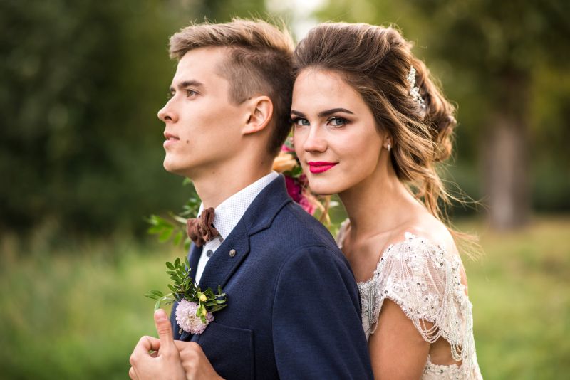 Bride and groom embracing in the park, look at camera